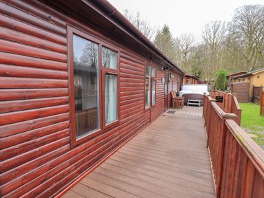A wooden deck with chairs and a hot tub outside a log cabin at Brightwater Lodge White Cross Bay near Windermere