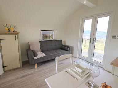 A living room with a gray sofa and a small green cabinet near glass double doors at Shepherds View in Castlerigg near Keswick