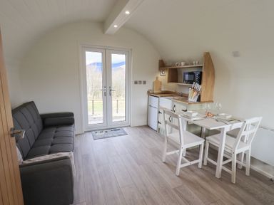 A small room with a gray sofa on the left a kitchenette with a microwave and knife set and a white dining table with two chairs at Shepherds View Castlerigg near Keswick