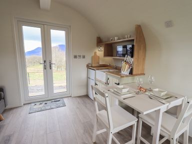 A small kitchen and dining area with a white table set for two and glass doors showing a mountain view at Shepherds View Castlerigg near Keswick