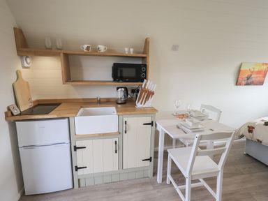 A small kitchen area with a fridge sink microwave knives and a dining table with two chairs at Shepherds View in Castlerigg near Keswick