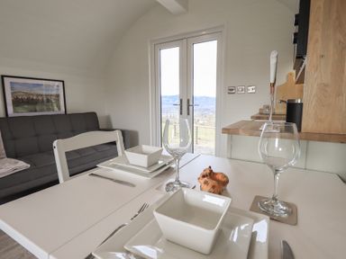 A dining table set with plates bowls and wine glasses next to a sofa and a kitchen area at Shepherds View in Castlerigg near Keswick