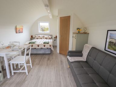 A living space with a bed near a window a dining table with chairs a gray sofa and a cabinet at Shepherds View in Castlerigg near Keswick