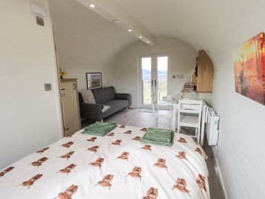A bedroom with a bed having a printed duvet and towels with a sofa dining table and chairs near glass doors at Shepherds View in Castlerigg near Keswick