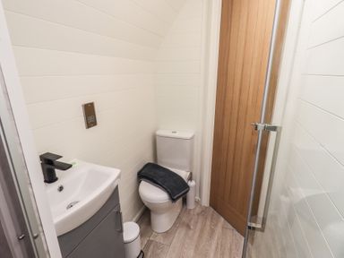 A small bathroom with a toilet and sink with faucet near a wooden door at Shepherds View Castlerigg near Keswick
