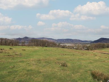 A grassy field with scattered bushes and trees with hills and a town in the background at Shepherds View in Castlerigg near Keswick
