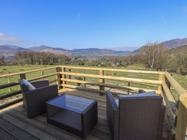 An outdoor wooden deck with two chairs and a glass top table overlooking fields and distant hills at Shepherds View in Castlerigg near Keswick