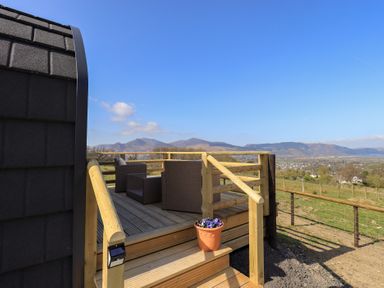 An outdoor wooden deck with wicker chairs and a table overlooking hills and fields at Shepherds View Castlerigg near Keswick