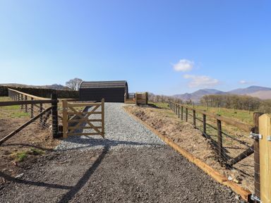 A gravel path leading through a wooden gate to a small black rounded cabin with fencing on both sides at Shepherds View in Castlerigg near Keswick