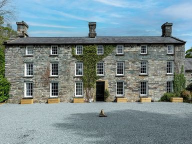 A stone building with multiple windows and a gravel driveway at Snowdonia Manor in Dolgellau