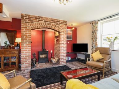 A living room with a brick fireplace wood stove leather chairs striped carpet and a television at Cobble Cottage in Great Ryburgh