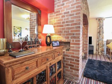 A wooden sideboard with a mirror lamp and cocktail shaker set next to a brick fireplace in a living room at Cobble Cottage in Great Ryburgh