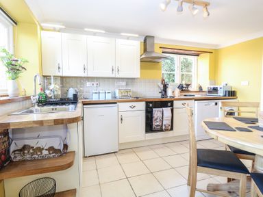A kitchen with white cabinets wooden countertops a sink a stove a dining table and yellow walls at Cobble Cottage in Great Ryburgh