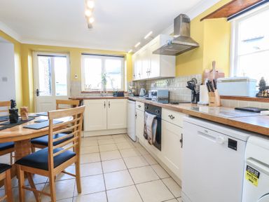 A kitchen with wooden countertops white cabinets a dining table with wooden chairs and tiled floor at Cobble Cottage in Great Ryburgh