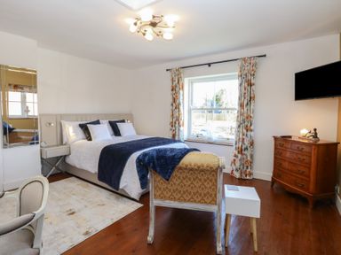 A bedroom with a bed a chair a wooden dresser and a window with curtains at Cobble Cottage in Great Ryburgh