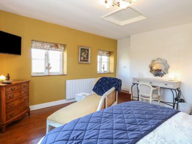 A bedroom with a bed a wooden dresser a chaise lounge a desk with a chair and two windows at Cobble Cottage in Great Ryburgh