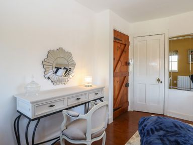 A bedroom corner with a white desk and chair mirror on the wall two doors and part of a bed at Cobble Cottage in Great Ryburgh