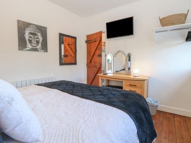 A bedroom with a bed a wooden dressing table with a mirror a wall-mounted television and a wooden door at Cobble Cottage in Great Ryburgh