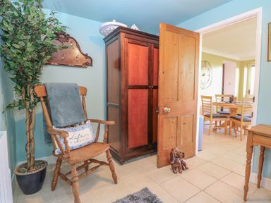 A room with a wooden chair, potted plant, wooden wardrobe, open door, and a dining area visible in the next room at Cobble Cottage Great Ryburgh