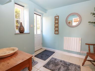 An entryway with a wooden table and chair two gray rugs a wall mirror and a white door at Cobble Cottage in Great Ryburgh