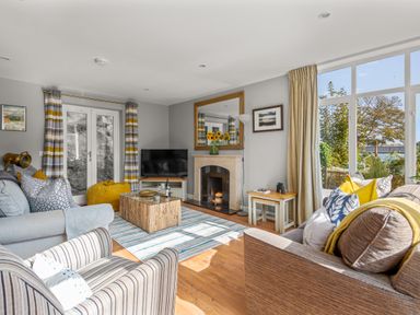 A living room with sofas a striped armchair a coffee table fireplace and large windows at Seascape in Kingsand