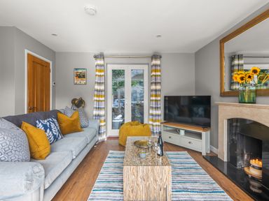 A living room with a sofa and cushions a coffee table a television and a fireplace at Seascape in Kingsand