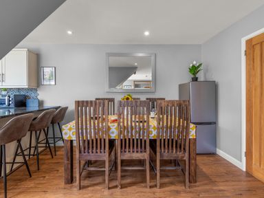 A dining area with a wooden table and chairs a refrigerator and bar stools at Seascape in Kingsand