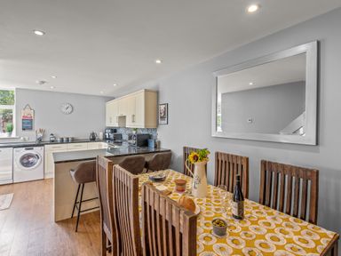 A kitchen and dining area with wooden chairs and a table with a yellow patterned tablecloth at Seascape in Kingsand