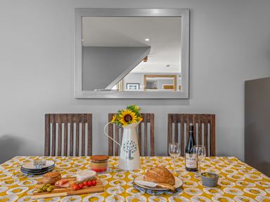 A dining table with food wine and flowers in a pitcher with wooden chairs and a mirror on the wall at Seascape in Kingsand