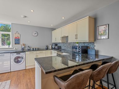 A kitchen with cream cabinets black countertops and three brown bar stools at Seascape in Kingsand