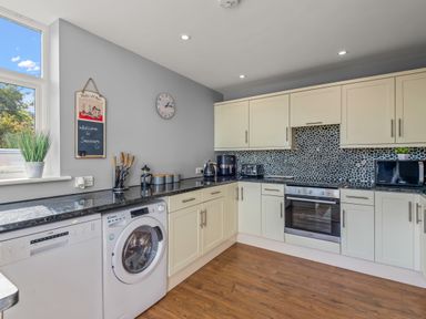 A kitchen with white cabinets black countertops a washing machine a dishwasher and a window at Seascape in Kingsand
