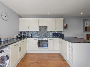 A kitchen with white cabinets black countertops a washing machine and various appliances at Seascape in Kingsand