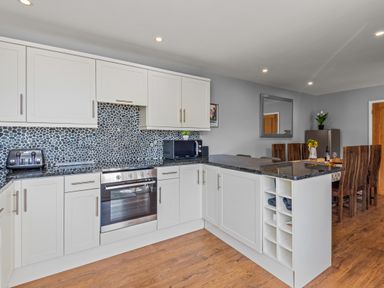 A kitchen with white cabinets black countertops a pebble tile backsplash and a dining table with wooden chairs at Seascape in Kingsand