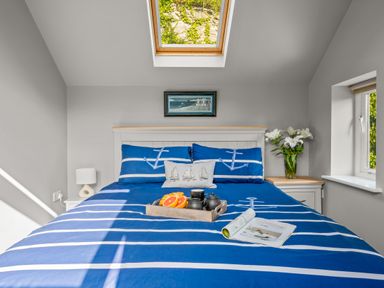 A bedroom with a bed covered in blue and white striped bedding with anchors on pillows and a skylight window at Seascape in Kingsand