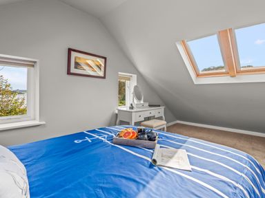 A bedroom with a blue bedspread a dressing table and skylight windows at Seascape in Kingsand