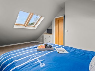 A bedroom with a blue striped bedspread a tray with breakfast on the bed a chest of drawers with a TV and a skylight window at Seascape in Kingsand