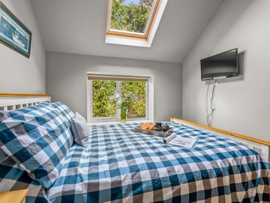 A bedroom with a checkered bedspread a tray with fruit and tea a wall-mounted tv and a window with flowers at Seascape in Kingsand