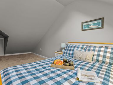 A bedroom with a blue and white checkered bedspread a tray with a teapot cups and fruit on the bed a nightstand with a lamp and a small painting on the wall at Seascape in Kingsand