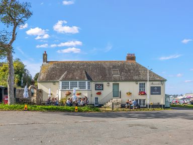 An outdoor seating area with tables and umbrellas next to a building with hanging flower baskets at Seascape in Kingsand