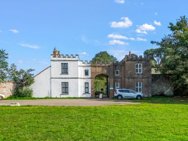 A castle gatehouse with two parked cars and a lawn in front at Seascape in Kingsand