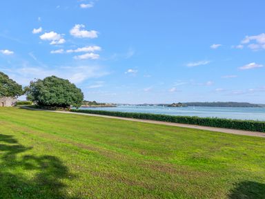 A grassy area with trees overlooking a body of water with boats and a distant shoreline at Seascape in Kingsand