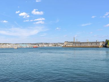 A large body of water with boats and buildings along the shore under a blue sky at Seascape in Kingsand