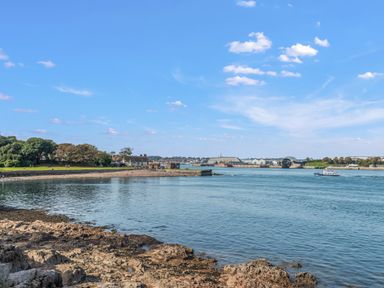 A coastal scene with rocky shoreline and water with buildings and trees in the background at Seascape in Kingsand