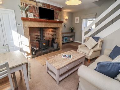 A living room with a wood stove in a brick fireplace a wooden coffee table armchairs and a dining table at Aln Cottage Alnmouth