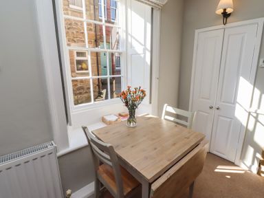 A small dining area with two chairs a wooden table and flowers on it near a window at Aln Cottage in Alnmouth