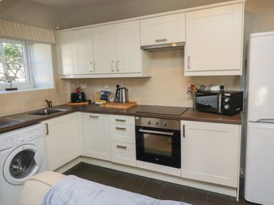 A kitchen with white cabinets a washing machine an oven a microwave and a refrigerator at Aln Cottage Alnmouth
