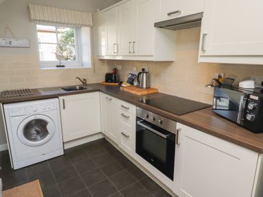 A kitchen with white cabinets a washing machine a sink an electric stove an oven a microwave and a kettle at Aln Cottage Alnmouth