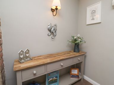A hallway with a wooden console table holding a vase with flowers and decorative candle holders with seahorse wall decor and framed lobster art at Aln Cottage Alnmouth