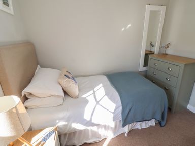 A bedroom with a single bed a blue blanket a chest of drawers with a mirror and a lamp at Aln Cottage Alnmouth