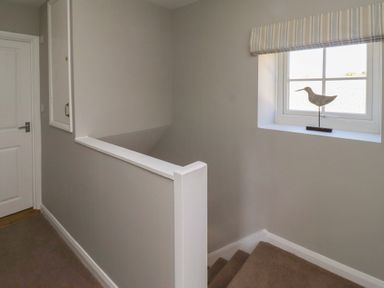 A staircase with beige carpet and a window with a bird decoration on the windowsill at Aln Cottage Alnmouth